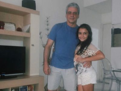 Gabriela Moura and her father are side hugging each other as they are posing for a picture.